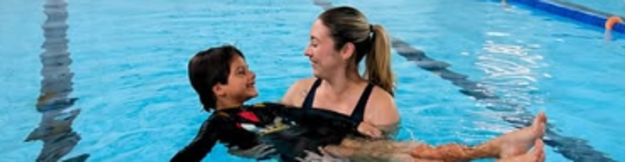 Terapeuta e criança sorrindo durante atendimento de hidroterapia na piscina do Instituto Therapy.